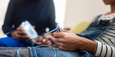 Closeup of teenage girl holding zapper electrodes with bioresonance therapist in background.