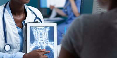 African american practitioner doctor holding tablet computer with medical radiography discussing xray expertise with sick patient during clinical appointment. Physician working in hospital office